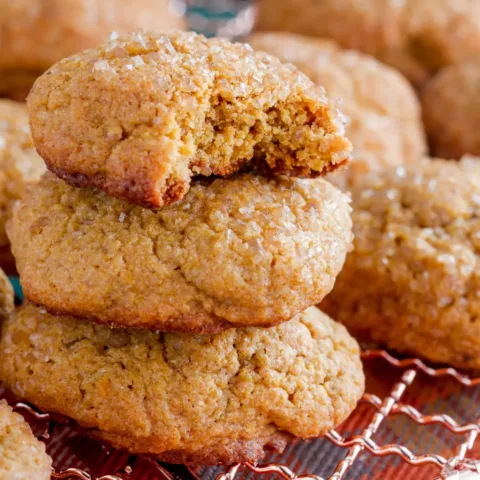 A stack of soft and chewy cinnamon sugar cookies on a wire rack. One cookie has a bite taken out of it, revealing its warm, golden interior.