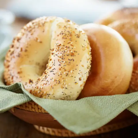 Freshly baked low calorie bagels topped with everything seasoning in a basket lined with a green napkin