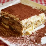 Close-up of a rich, creamy tiramisu brownie dusted with cocoa powder on a white plate