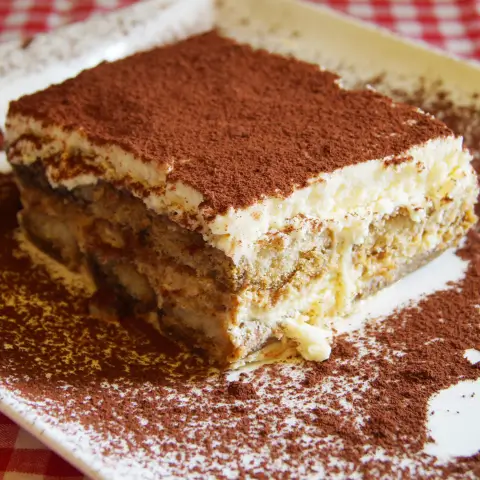 Close-up of a rich, creamy tiramisu brownie dusted with cocoa powder on a white plate