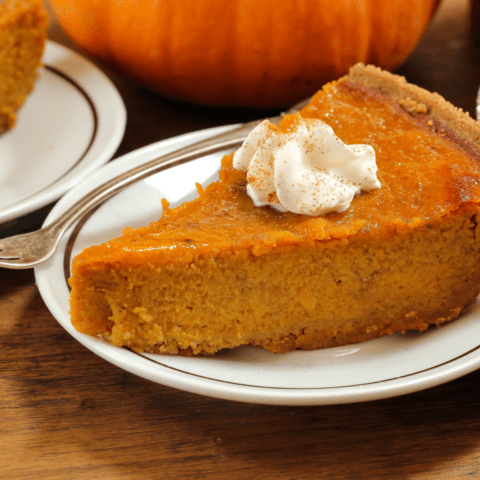 A slice of pumpkin pie with a generous dollop of whipped cream and a sprinkle of cinnamon