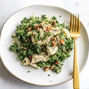 A fresh and vibrant Green Goddess Tuna Salad served on a plate with a golden fork, featuring chopped kale, flaked tuna, a creamy herb dressing, and crunchy nuts.