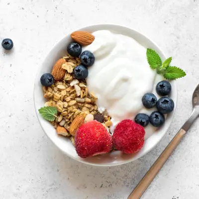 A bowl of yogurt parfait topped with granola, almonds, blueberries, and strawberries.
