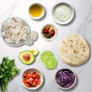 A vibrant and colorful arrangement of fresh ingredients for cauliflower tacos, featuring roasted cauliflower florets, sliced avocado, chopped cilantro, diced red onion, lime wedges, and corn tortillas on a rustic wooden surface, bright and inviting natural lighting.
