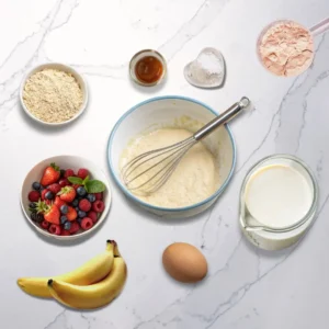 Healthy protein pancakes breakfast ingredients: protein powder, fresh berries, bananas, and whole-wheat flour.