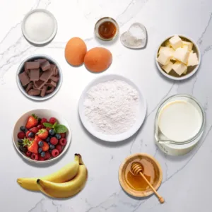 Ingredients for banana crepes, including bananas, flour, eggs, milk, butter, berries, honey, and chocolate