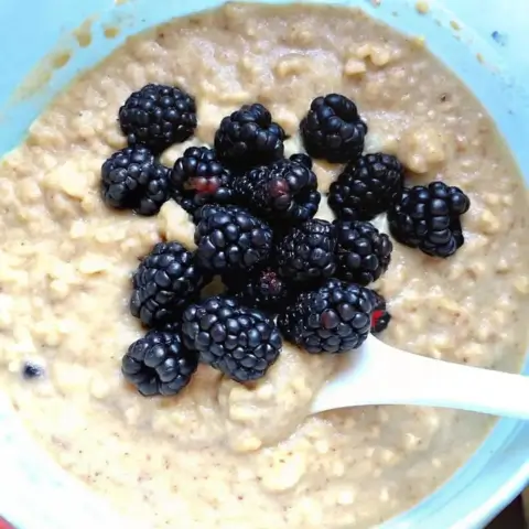 Close-up of creamy banana oatmeal muffin batter topped with fresh blackberries in a mixing bowl.